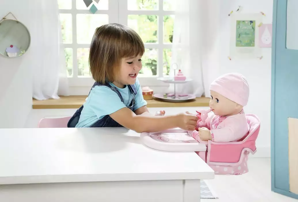 Ilustracja: dziewczynka karmi laleczkę siedzącą w krzesełku dla lalki przy stole Baby Annabell
