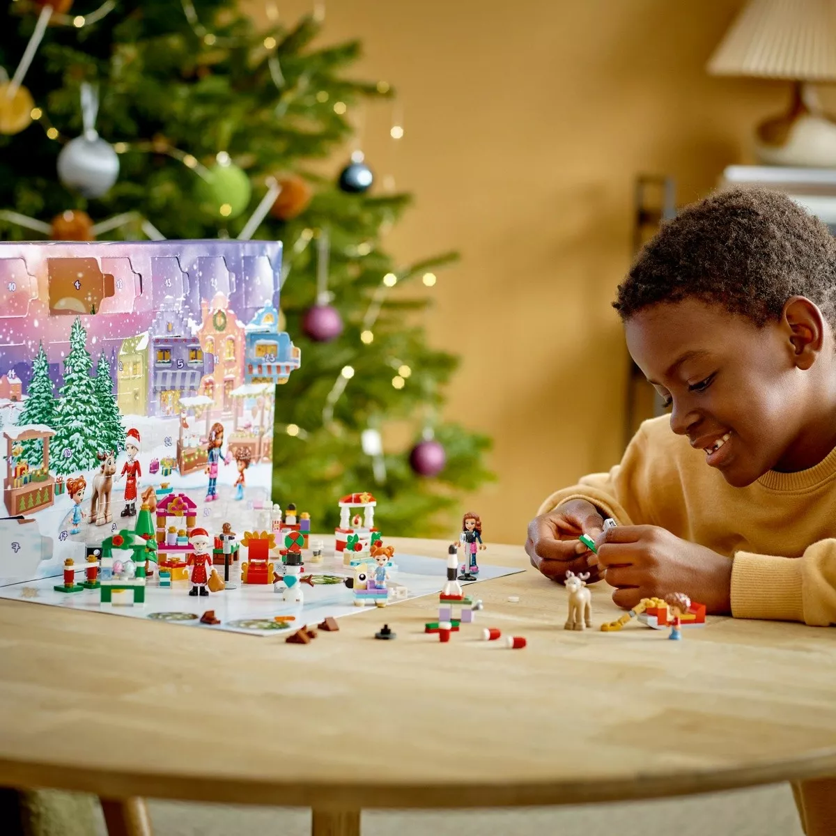 Ilustracja: chłopiec rozpakowuje kalendarz adwentowy LEGO 2022, z tyłu choinka